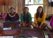 Calleria women sit smiling in front of their handwoven textiles